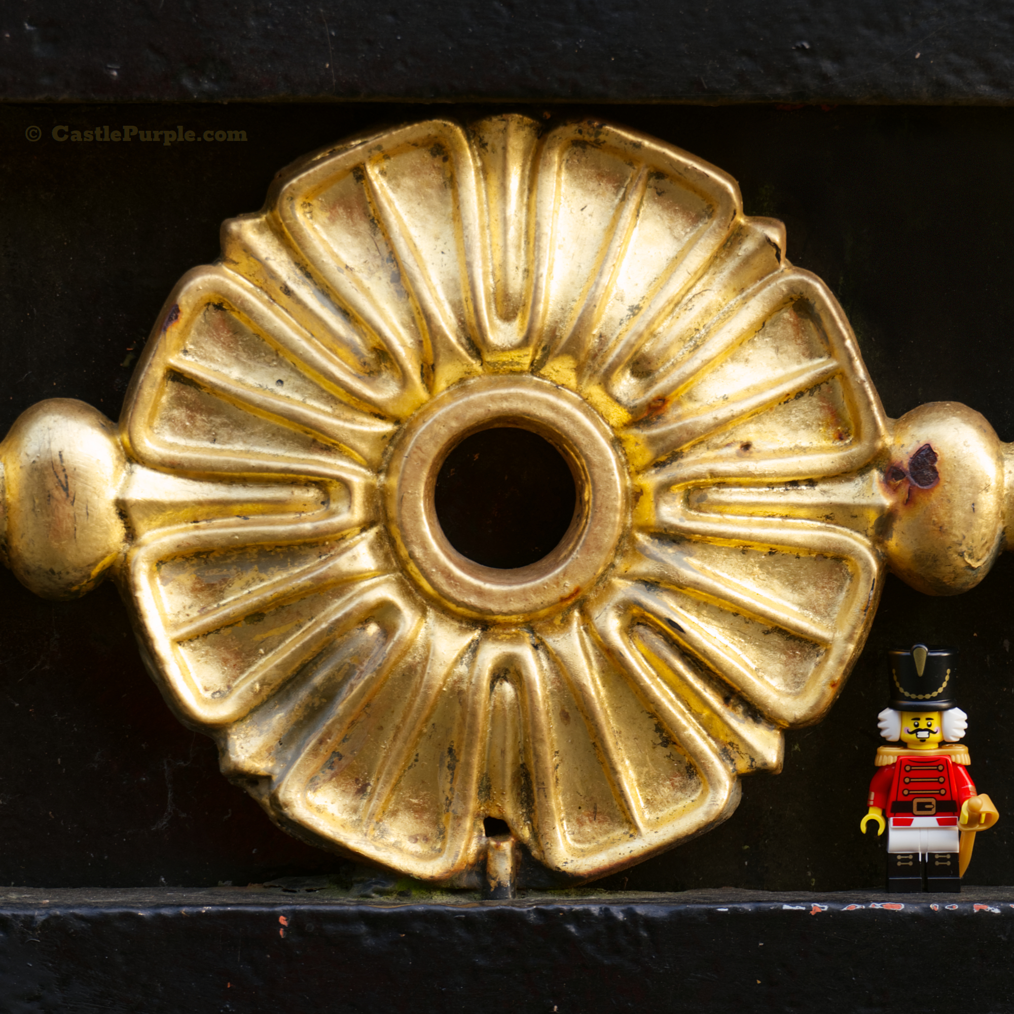 the Lego Nutcracker minifigure pictured next to a shiny gold metal decorative flower (part of a metal gate).