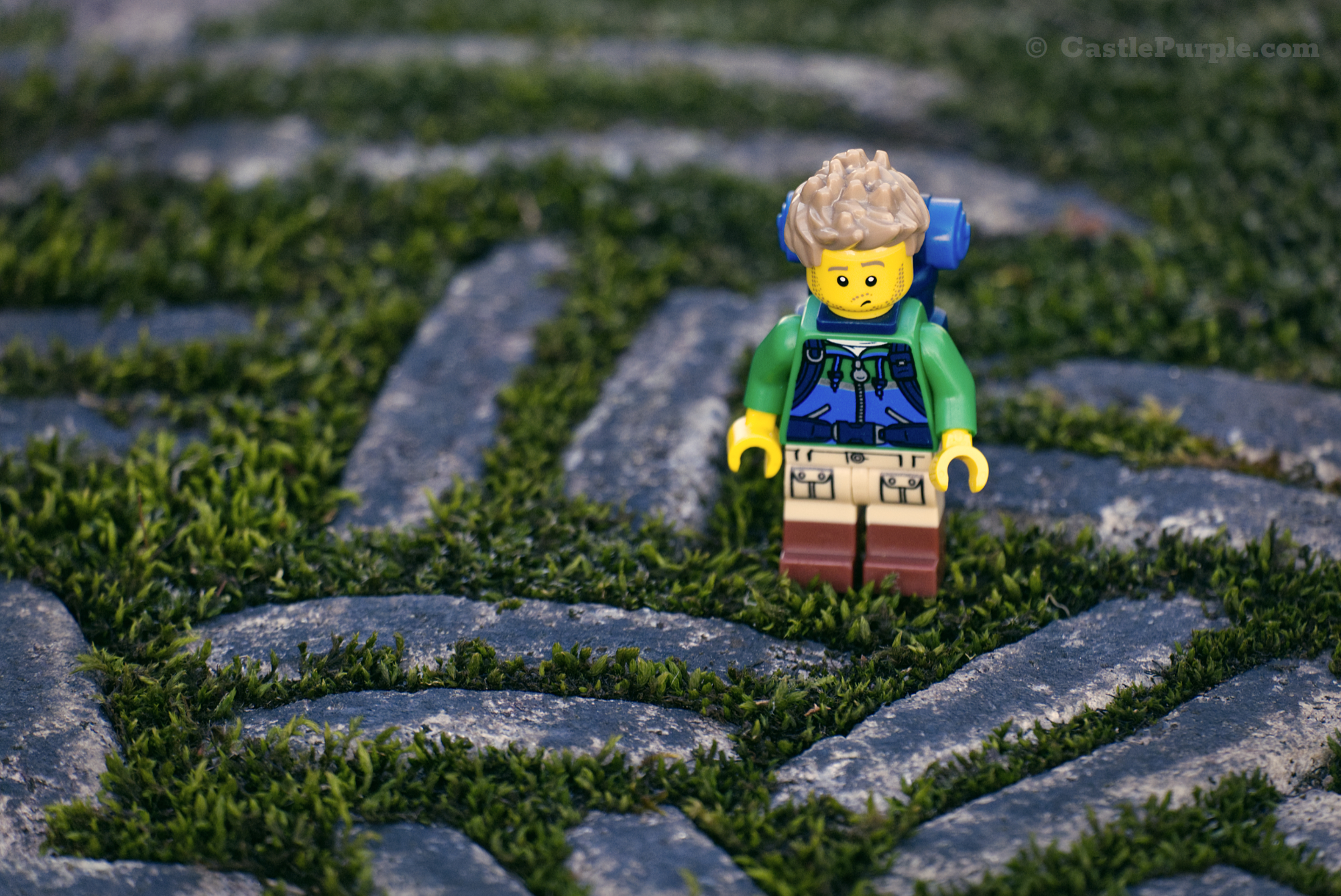 The Lego hiker minifigure stands on the ground surrounded by some raised stone markings with grass in between